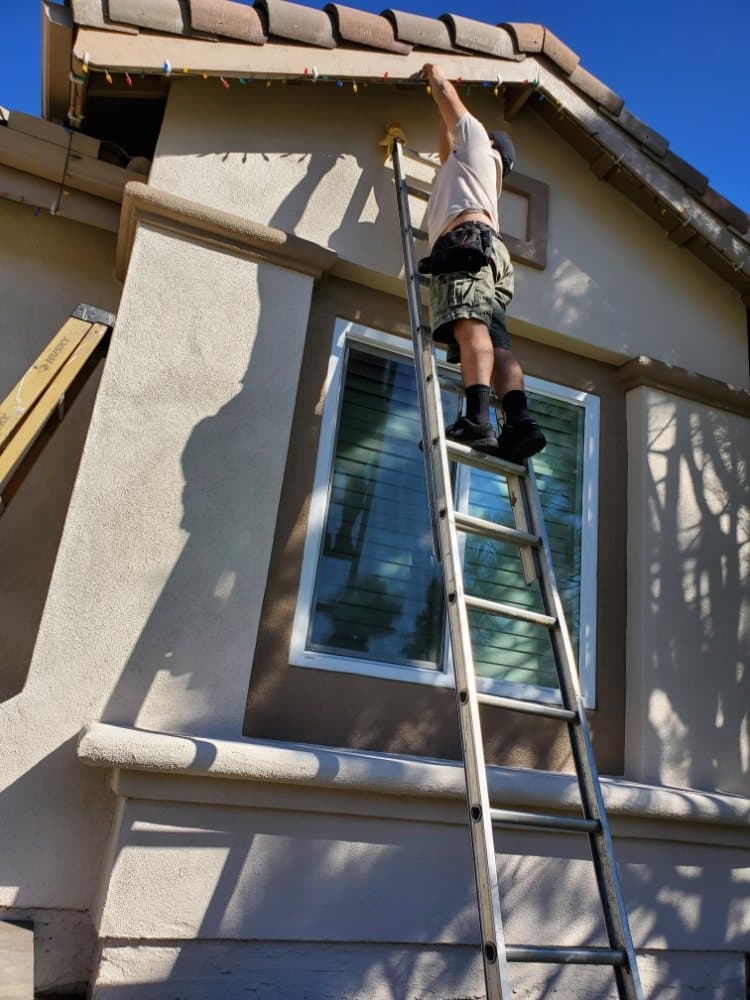Raul on a ladder hanging holiday lights
